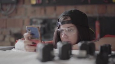 Portre genç kadın mobilya üretiminde cep telefonu bakmak ve birisi yüzüne kompresör bir atış vermek