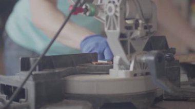 Ön planda küçük dairesel testere yakın. Adam, arka planda çalışmalarını yaparken koruyucu eldivenler giydirdi. Mobilya fabrikasında çalışma süreci. Marangoz mesleği