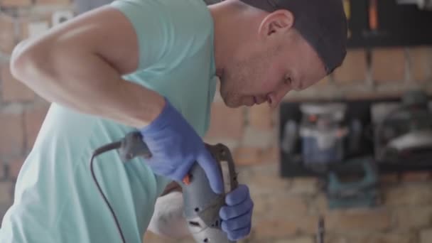 Porträt eines Ingenieurmeisters, der vor dem Hintergrund einer kleinen Werkstatt ein Loch mit Werkzeug bohrt. Konzept der Handfertigung. Handwerker arbeitet in einer Werkstatt. — Stockvideo