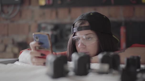 Portre genç kadın mobilya üretiminde cep telefonu bakmak ve birisi yüzüne kompresör bir atış vermek — Stok video