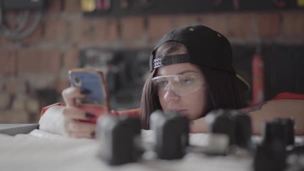 Retrato de mujer joven mira el teléfono móvil en la fabricación de muebles y alguien le da una oportunidad de compresor en la cara — Vídeos de Stock