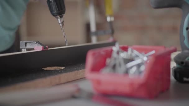 Unbekannter Tischler fertigt mit Akku-Schraubendreher Hallen in Spanplatten. Konzept der Handfertigung. Handwerker arbeitet in einer Werkstatt. — Stockvideo