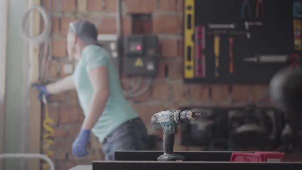 Retrato de carpintero profesional cortando un trozo de madera en su taller de carpintería, utilizando una sierra circular con otra maquinaria en el fondo. Concepto de fabricación manual. Artesano trabaja en un — Vídeo de stock