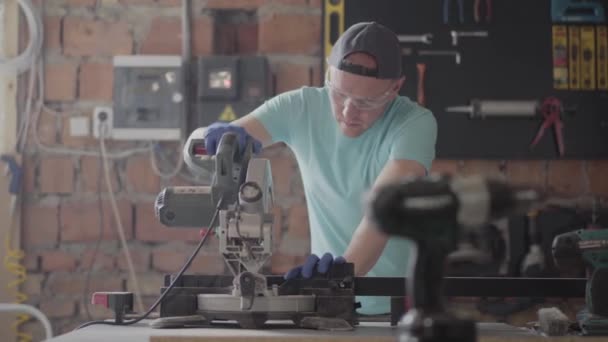 Portret rzemieślnika w okularach ochronnych cięcie drewnianej deski z małą piłą tarczową na stole w warsztacie. Fabryka mebli. Koncepcja produkcji ręcznej. CraftMan pracuje w warsztacie. — Wideo stockowe