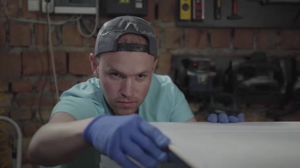 Retrato del hombre concentrado en la tapa, involucrado en su trabajo. El trabajador con guantes comprobando y midiendo su bricolaje. Profesión del carpintero. Concepto de fabricación manual. Artesano trabaja en un — Vídeo de stock