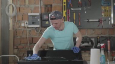 Eldivenli marangoz yıkama ayna yüzeyi Craftsman yansıması. Bir adam spreyin yüzeyine sıçratıyor. El üretim kavramı. Mobilya üretimi. Craftman bir atölyede çalışıyor.