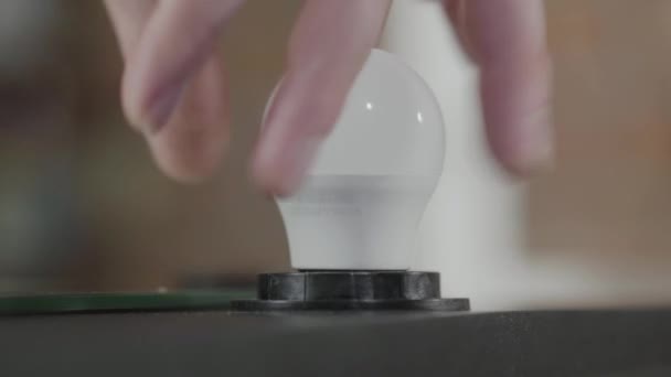 Primo piano di mano maschile avvitare una lampada all'interno di una lampadina e la sua luce. Produzione manuale. Artigiano lavora in un laboratorio . — Video Stock