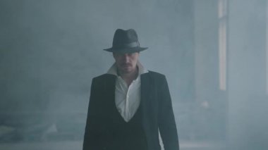 Fedora şapka ve klasik takım elbise portre emin acımasız gangster dumandan yürümek. Yavaş çekim. Terk edilmiş harap bina. Kendine güvenen işadamı rahatlatıcı.
