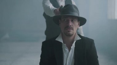 Portre emin kötü adam fedora şapka ve diğer adam bir silahla arkasından yürüyen sandalyeye oturup ve kafasına ateş. Arkadan gelen ve silahı mans kafasına dayayan tanınmayan adam.
