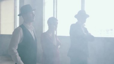 Üç gangster, fedora şapkalı iki adam ve klasik takım elbiseli iki adam ve 1950'de kadın kirli yerde duman lar içinde duruyor ve kadın silahtan ateş ediyor. Terk edilmiş harap bina.