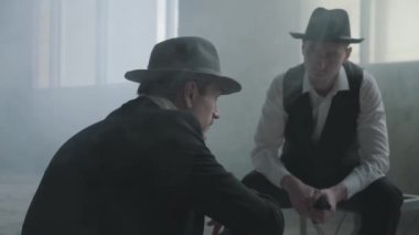 Terk edilmiş bir binada oturup iş tartışan şapkalı iki şık adamın portresi. Mafya adamları boş bir binada buluşuyorlar. Havalı adamlar, haydutlar, mafya, suç çetesi. Terk edilmiş harap