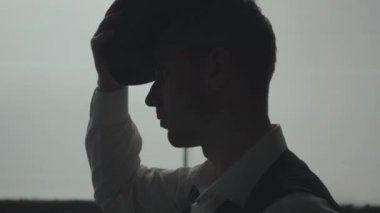 Yakışıklı kendine güvenen adamın büyük pencerenin önünde kafasına şapka takmasının yan görünümü. Mafyanın başı toplantıya hazırlanıyor. Ceza dairesi portresi. Kendine güvenen işadamı rahatlatıcı