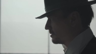 Büyük pencerenin önünde tehditkar bakışlarla şapkayı çıkaran yakışıklı kendine güvenen adamın yan görünümü. Mafyanın başı muhatabın gözünü korkutuyor. Ceza dairesi portresi, yakın çekim