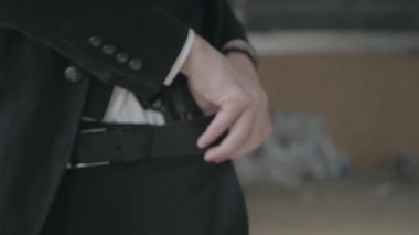 Takım elbiseli tanınmayan adam ceketi geri iter ve kemerin arkasına gizlenmiş silahı gösterir ve sonra tekrar kapatır. Ceza dairesi, mafya, suç çetesi, havalı adam