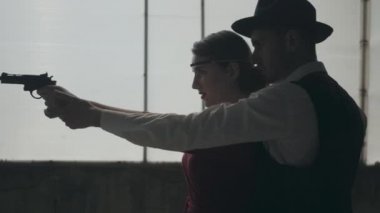 Kırmızı elbiseli portre zarif genç kadın bir silah nişan, yakışıklı yiğit adam arkasında duruyor, elini yönlendiren, yan görünüm. Mutlu gangsterler. Bonnie ve Clyde