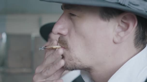 Двое мужчин в шляпе в фетровой шляпе стоят серьезно и страшно курят сигарет — стоковое видео