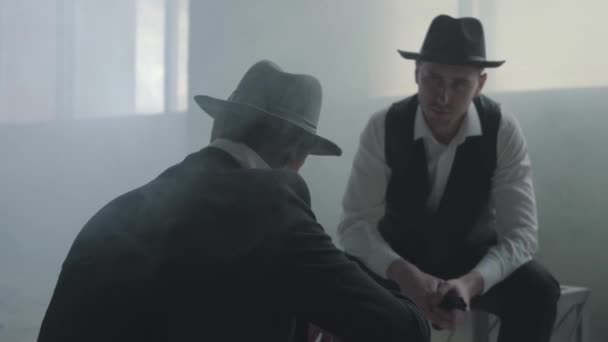 Two stylish men in hats sitting in an abandoned building discussing business. The mafia guys have meeting in an empty building. Cool guys, thugs, mafia, criminal gang. Abandoned dilapidated building. — Stock Video