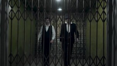 Resmi takım elbiseli ve forfektos şapkalı iki gangsterin metal sahte kapılar açması portresi