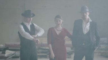 Terk edilmiş bir binada kameraya tabanca doğrultan kırmızı elbiseli bir kadının iki yanında duran kendine güvenen iki iyi giyimli adamı portre. Havalı adamlar, haydut, mafya, suç çetesi