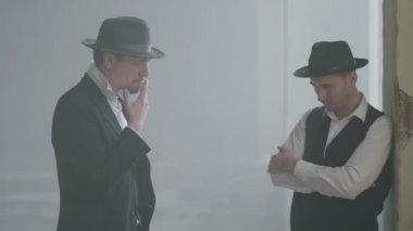 Fedora şapkalı iki kendinden emin yetişkin adam kırık durty yerde ayakta ve konuşuyor. Terk edilmiş harap bina. Kendine güvenen bir işadamı rahatlatıcı. Mafya klanı. Suç gruplandırma.