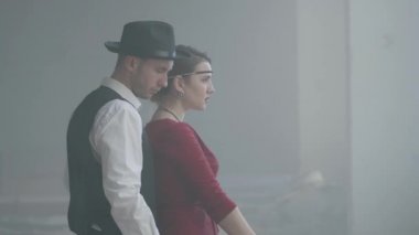 Kırmızı elbiseli zarif genç kadın yavaş yavaş bir silah nişan, yakışıklı yiğit adam arkasında duruyor, elini yönlendiren, yan görünüm. Mutlu gangsterler. Bonnie ve Clyde. Yan görünüm