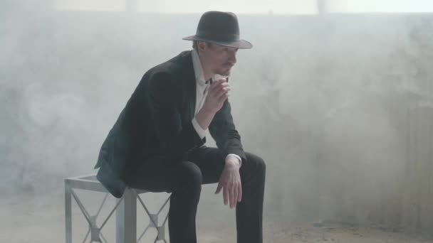 Retrato belo homem confiante em um chapéu vomita e pega a moeda sentada em um prédio abandonado. O chefe da máfia está à espera num edifício vazio. Edifício abandonado em ruínas . — Vídeo de Stock