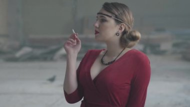 Portre kendine güvenen genç kadın eski tarz kumaş ateş sigaret. Terk edilmiş harap bina.