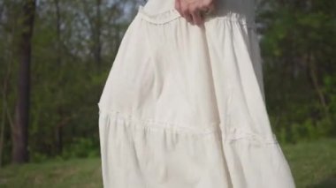 Uzun beyaz etek ve kot ceket ile cep telefonu ile güzel kadın yakın ormanda yürüyüş. Kamera yukarı doğru hareket ediyor. Yan görünüm. Yaz leasure. Yavaş çekim
