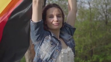 Portre güzel kendinden emin kadın el kaldırdı Alman bayrağı tutan. Bayrak rüzgarda dalgalı. Alman vatandaşı ülkesinin vatanseveridir. Açık hava rekreasyon.