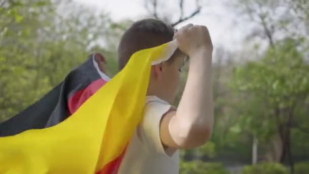 Colegial corriendo por el parque con la bandera negra-roja-amarilla de Alemania ondeando detrás. Movimiento lento — Vídeo de stock