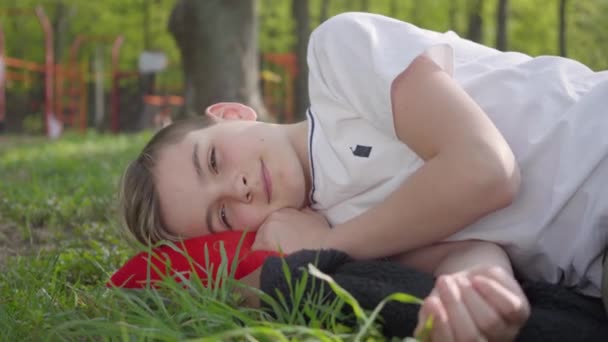 春天公园里一个可爱的男孩躺在绿草地上的肖像。户外娱乐. — 图库视频影像