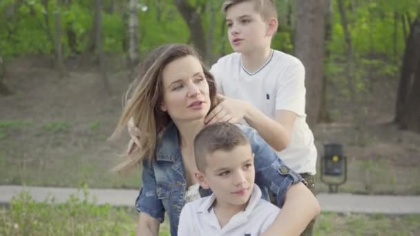 Porträt einer süßen jungen Mutter mit kleinen entzückenden Kindern, die sich im Park ausruhen. Freizeitgestaltung im Freien. — Stockvideo