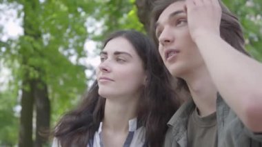 Portre güzel genç çift aşık rahat giysiler bankta konuşurken oturan ve el ele tutuşarak giyiyor. Mutlu kız ve erkek parkta birlikte vakit geçiriyorlar. Açık havada boş zaman
