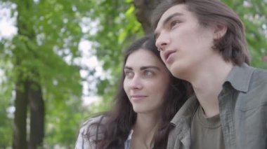 Portre güzel genç çift aşık rahat giysiler bankta konuşurken oturan ve el ele tutuşarak giyiyor. Mutlu kız ve erkek parkta birlikte vakit geçiriyorlar. Açık havada boş zaman