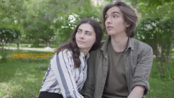 Retrato joven pareja en ropa casual sentada en el banco hablando y tomados de la mano. Chica feliz y chico pasando tiempo juntos en el parque. Ocio exterior — Vídeos de Stock