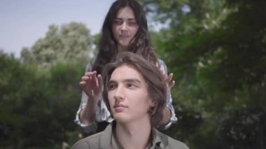 Ön planda oturan parantez ve uzun saçlı Portre yakışıklı genç adam, kız arkadaşı arkasından geliyor ve gözlerini kapamak. Adam ona bakıyor. Güzel çiftin parkta bir randevusu var.