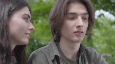 Sıradan giysiler içinde portre güzel genç çift parkta birlikte vakit geçirmek, bir tarih sahip. Adam şaka yapıyor ve kız mutlu bir şekilde gülüyor. Dışarıda boş zaman, yaz saati. Kamera hareket ediyor