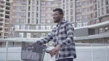 Portre yakışıklı Afro-Amerikan adam kentsel mimarinin arka plan karşı bisiklet ile ayakta. Adam dışarıda iyi havalarda dinleniyor.