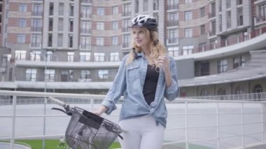 Şehir mimarisinin arka planına karşı bisiklet le ayakta bisiklet kask Pretty sarışın kadın. Bayan şehirde bisiklet yolunda. Aktif yaşam tarzı. Kamera yaklaşıyor