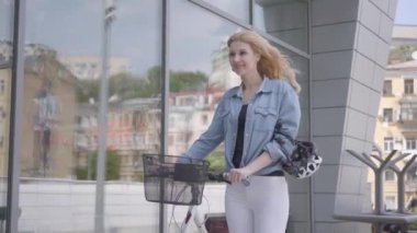 Portre sevimli genç ince çekici sarışın kadın beyaz kot şehirdeki vitrinler yakınında onu bisiklet lider. Sıcak bayan açık havada vakit geçiriyor, aktif yaşam tarzı. Kamera aşağı hareket ediyor