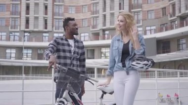 Yakışıklı Afro-Amerikan adam çekici bir sarışın kadın ile konuşurken kentsel mimarinin arka plan karşı bisiklet ile ayakta. Birkaç arkadaş dışarıda sohbet ediyor. Uluslararası dostluk