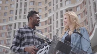 Çekici kadın ile konuşurken kentsel mimarinin arka planına karşı bisiklet ile yakışıklı güvenen Afrikalı Amerikalı adam Portresi. Birkaç arkadaş dışarıda sohbet ediyor. Uluslararası