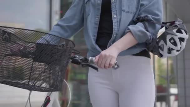 Joven mujer rubia atractiva delgada en jeans blancos que lleva su bicicleta cerca de los escaparates de la ciudad. La mujer caliente pasar tiempo al aire libre, estilo de vida activo. Cámara subiendo — Vídeo de stock