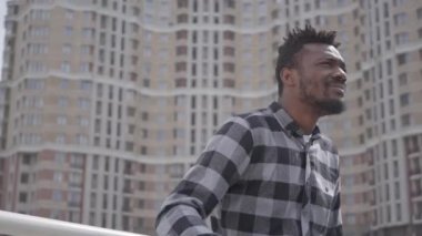 Şehir mimarisinin arka planına karşı duran yakışıklı Afro-Amerikan bir adamın portresi. Adam iyi havalarda açık havada dinleniyor, arka planda gökdelen