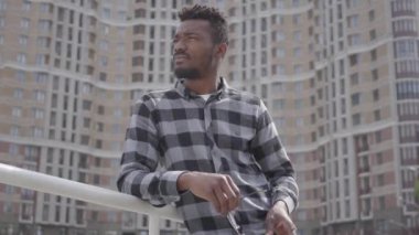 Confidient yakışıklı Afro-Amerikan adam portre güneş gözlüğü koyarak kentsel mimarinin arka plan karşı ayakta. Dışarıda tek başına dinlenen adam, arka plandaki gökdelen.