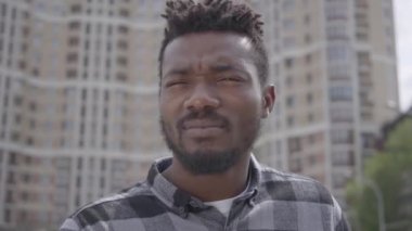 Güneşte şaşı lık lakaplı kentsel binanın arka planına karşı duran, sonra da güneş gözlüğü takan afro-Amerikan bir adamın yakın yüzü. Dışarıda tek başına dinlenen adam, gökdelen.