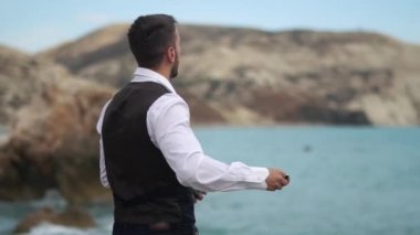 Denize ve dağlara yakın, suya taş atan yakışıklı genç bir adam. Yavaş çekim. Kıbrıs. Baf