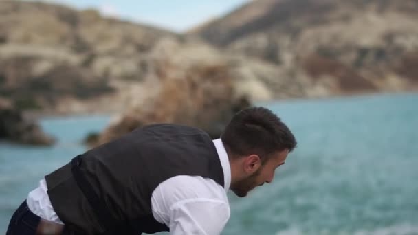 Pria berjenggot melempar batu ke laut. Gerakan lambat. Siprus. Pafos — Stok Video