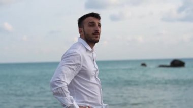 Genç sakallı adam etrafına harika bir deniz manzarası bak. Beyaz klasik gömlek giyen adam, çok şık ve yakışıklı. Genç adam deniz kıyısında huzur içinde duruyor. Kıbrıs. Papolar