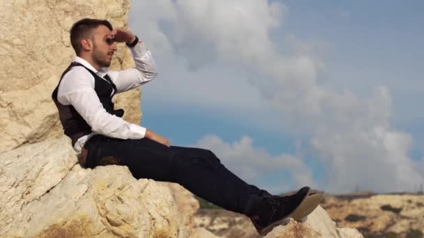 Gutaussehender, stilvoller Mann in schickem Tuch, der auf den Felsen am Meer sitzt. Zypern. Paphos — Stockvideo